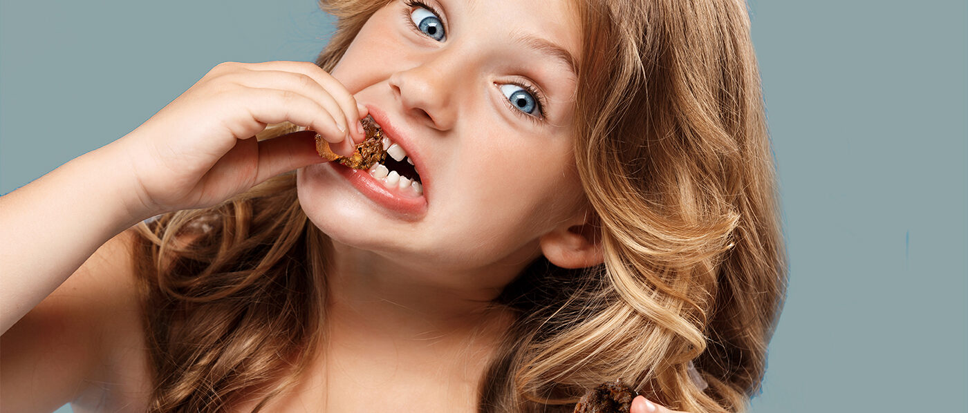 Young pretty girl eating strawberry, looking at camera over blue background. Copy space.