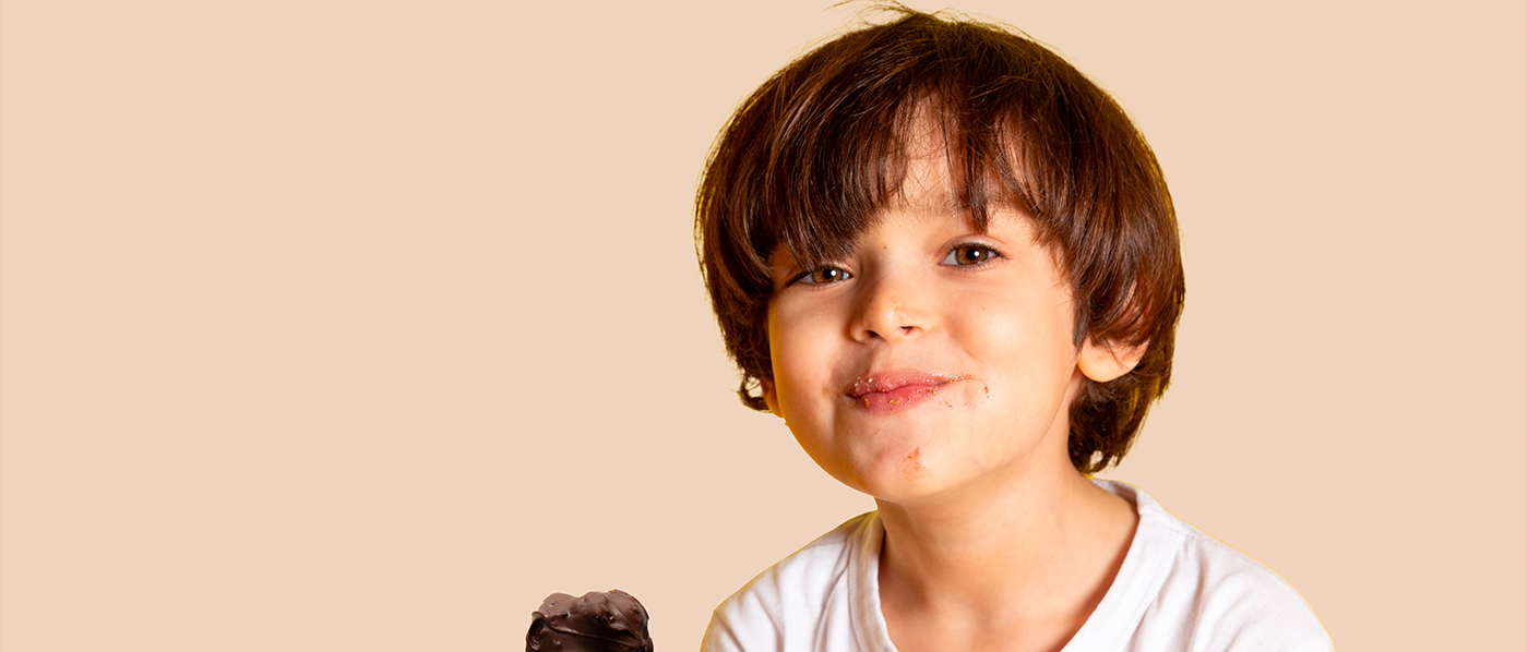 Close up shot of cheerful curly haired woman keeps mouth widely opened bites delicious macaroon enjoys eating sweet food has sugary addiction isolated over pink background. Confectionery concept